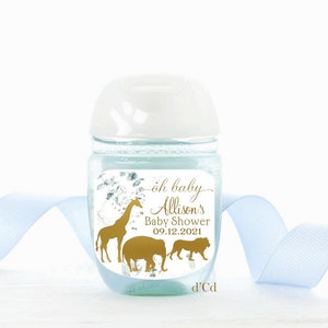 May include: A white hand sanitizer bottle with a clear label featuring a gold giraffe, elephant, and lion. The label also includes the text "oh baby Allison's Baby Shower 09.12.2021" and "d'Cd".