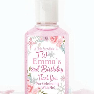 May include: Pink hand sanitizer bottle with a white cap and a label featuring floral and snowflake designs. The label reads "A Little Snowflake Is, TW Emma's 2nd Birthday, Thank You, For Celebrating With Me!"