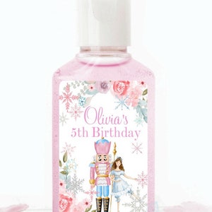 May include: Pink hand sanitizer bottle with a white label featuring a watercolor illustration of a nutcracker and a ballerina. The label also includes the text "Olivia's 5th Birthday" and a floral design.