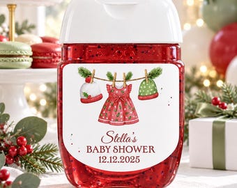 May include: A clear plastic hand sanitizer bottle filled with red gel, featuring a white label with a watercolor illustration of a red dress, a white hat, and a green hat hanging on a clothesline. The text reads Stella's BABY SHOWER 12.12.2025.