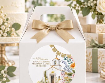 May include: A white gable-top favor box featuring a gold satin ribbon bow and a circular sticker. The sticker displays a watercolor illustration of a mission-style church, cacti, and flowers with the text: Welcome TO OUR WEDDING ANA MÁRIA Y ARRON 12.02.2025.