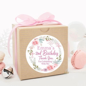 May include: A round, white sticker with a pink floral wreath and snowflakes. The sticker says "Emma's 2nd Birthday Thank You. For Celebrating With Me!"