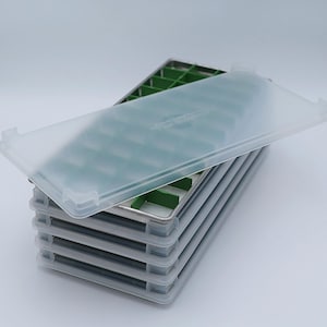 May include: A stack of five clear plastic ice cube trays with green silicone inserts. The top tray has a clear plastic lid.