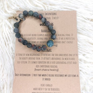 May include: A black and green beaded bracelet with a red and gold bead. The card reads "Soulful Intentions, High Vibrational Jewelry, Bloodstone: An excellent blood cleanser and a powerful healing stone. It eases creativity, courage and intuition. It has a protective that draws off negativity and grounds one's energy [root chakra healing]. Moss Agate: A stone of new beginnings. It refreshes the soul and opens one up to the beauty around them. It attracts abundance in wealth and self-esteem. Its slower vibration has a very grounding effect and aids emotional healing [heart chakra healing]. Daily Affirmation: I trust that when I release resistance my life flows as it should. Reiki-charged, Made with love in the Berkshires, www.soulfulintentions.etsy.com"