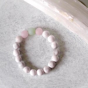 May include: A pink and green beaded bracelet with a light pink background.