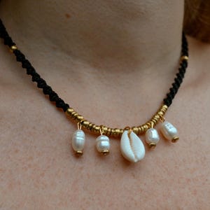 May include: A black cord necklace with gold beads and white shell and pearl charms.