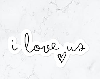 May include: A white sticker with the handwritten phrase "i love us" in black cursive script. A small heart icon is next to the word "us". The sticker is set against a white marble background.