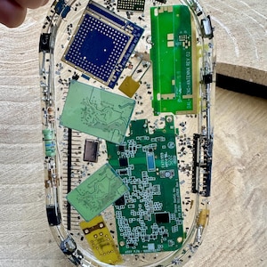 May include: Oval resin tray with embedded electronic components, including green and blue circuit boards, chips, and metallic flakes. The tray contains text that reads "DAL-ENG MODEM REV" and "DAL-ENG-ANTENNA REV 02".