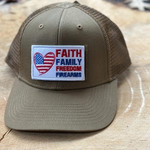 May include: A green and brown trucker hat with a patch that says "Faith Family Freedom Firearms" and a red, white, and blue heart with stars.