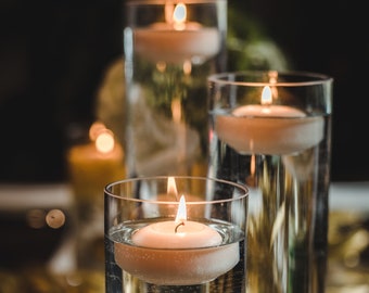 May include: Three glass candle holders with floating candles. The candles are white and the holders are clear glass. The candles are lit and the flames are visible.