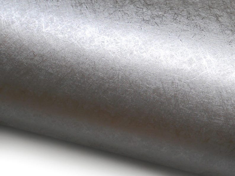 May include: Close-up of a roll of silver metallic textured paper. The paper has a subtle, irregular pattern with a slightly reflective surface. The paper is rolled up, revealing its texture and color.