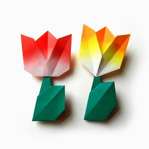 Op de afbeelding: Twee origami tulpen, één rood en wit, de andere geel en wit, met groene stelen.