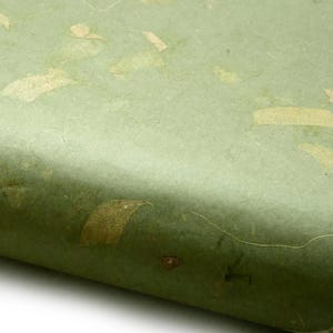 Könnte beinhalten: Nahaufnahme von handgefertigtem grünem Papier mit eingebetteten Gold- und Beigetönen. Das Papier hat eine strukturierte Oberfläche und eine leichte Krümmung, die seine Dicke erkennen lässt. Wahrscheinlich für Bastelarbeiten, Schreibwaren oder Kunstprojekte verwendet.