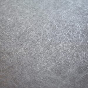 May include: Close-up of a textured, gray surface with a fibrous appearance. The surface has a subtle, mottled effect with fine, light-colored strands scattered across it, creating a soft, almost ethereal look. The overall tone is neutral and muted.