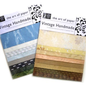 May include: Two packs of "Vintage Handmade" Japanese paper. Each pack contains nine decorative paper pieces. One pack features blue and gray tones, while the other has yellow, brown, and copper hues. The packaging includes the text "the art of paper."