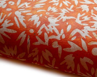 May include: Close-up of textured orange paper with a white floral pattern. The paper has a slightly crumpled appearance, with the white design creating a contrast against the warm orange background. The paper is rolled.