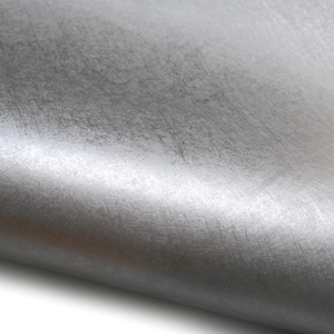 May include: Close-up of a roll of silver-colored fabric. The material has a textured surface with subtle variations in tone, creating a metallic sheen. The fabric is slightly curved, revealing its flexible nature.