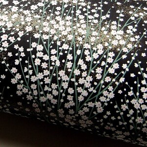 May include: Black wrapping paper with a white floral pattern. The flowers are small and delicate, and they are arranged in a random pattern. The paper has a subtle sheen.