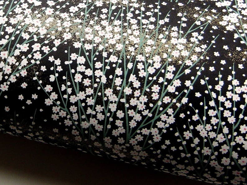 May include: Black wrapping paper with a white floral pattern. The flowers are small and delicate, and they are arranged in a random pattern. The paper has a subtle sheen.