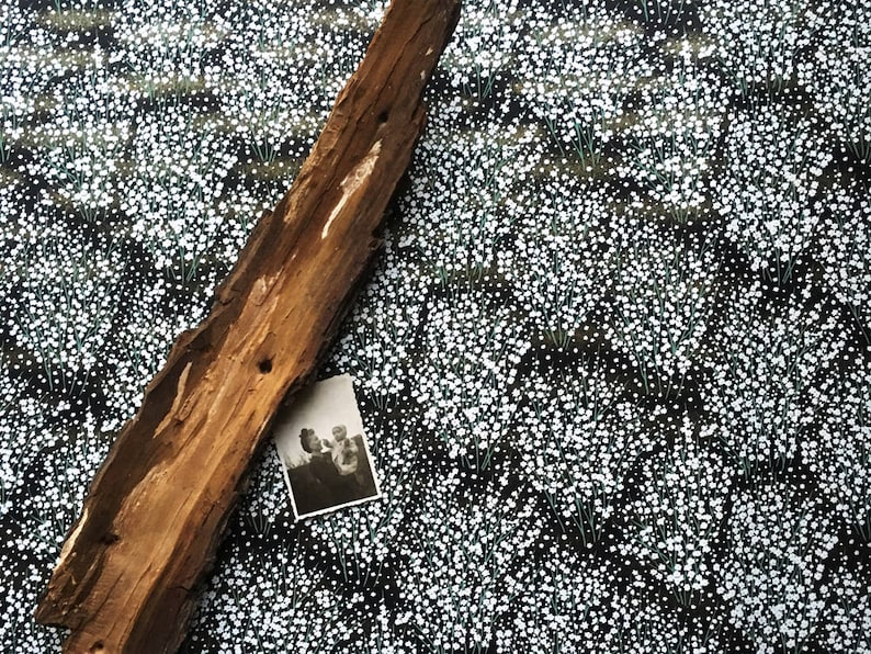 May include: A weathered piece of driftwood lies on a black background with a white floral pattern. A black and white photograph of two people is tucked under the driftwood.