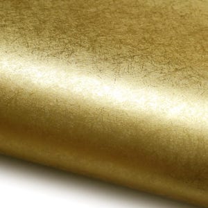 Pode incluir: Close-up de um rolo de papel dourado texturizado. O papel tem um brilho metálico e um padrão sutil e irregular. A superfície reflete a luz, criando destaques e sombras. O papel é provavelmente usado para artesanato ou decoração.