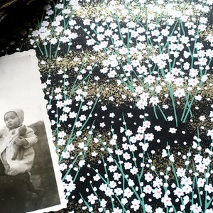 May include: A black and white photograph of a woman holding a baby. The woman is smiling and the baby is looking up at something. The photograph is on a black background with a white floral pattern.