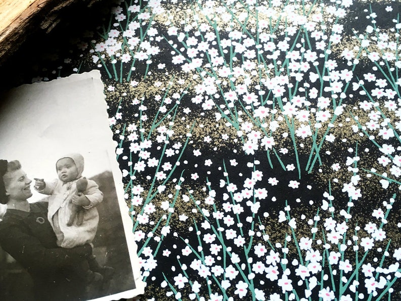 May include: A black and white photograph of a woman holding a baby. The woman is smiling and the baby is looking up at something. The photograph is on a black background with a white floral pattern.