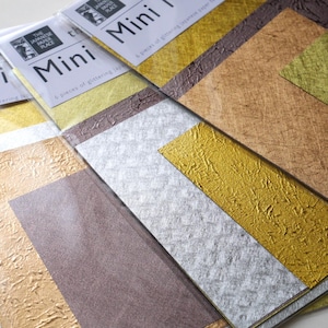 Può includere: Una collezione di fogli di carta giapponese scintillante in oro, argento e marrone. Ogni confezione è etichettata "Mini" e contiene sei pezzi di carta glitterata. La carta ha una finitura metallica e strutturata, ideale per lavori creativi e decorativi.