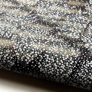 May include: Black fabric with a white floral pattern. The fabric is covered in small white flowers with green stems.