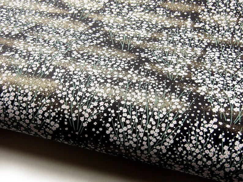 May include: Black fabric with a white floral pattern. The fabric is covered in small white flowers with green stems.