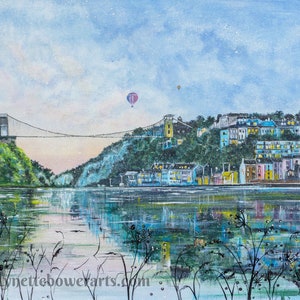 Peut inclure: Une peinture à l'aquarelle d'un pont suspendu au-dessus d'une rivière avec une ville de l'autre côté. Le pont est blanc et la ville est un mélange de couleurs pastel. Il y a deux montgolfières dans le ciel. La peinture est réalisée dans un style doux et rêveur.