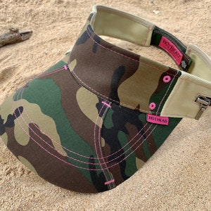 May include: Camouflage visor with pink stitching and a zipper detail. The visor has a beige band with the text "HOTHEAD" printed in pink.