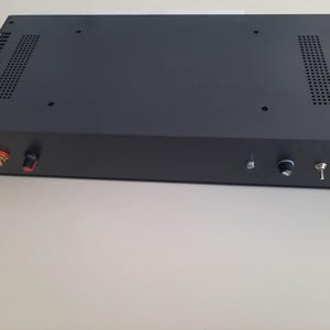 May include: Black metal box with a knob, switch, and two red and gold connectors on the front. The box has a black metal grill on the top and bottom.