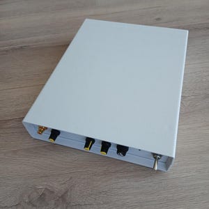 May include: A rectangular, light grey electronic device with several black and yellow knobs and a silver switch. The device has gold-coloured connectors and is set on a wooden surface.