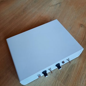 Op de afbeelding: Een witte doos met drie zwarte knoppen en twee kleine zilveren schakelaars. De doos staat op een houten oppervlak.