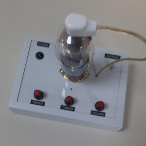 May include: A white radio with a glass vacuum tube, three knobs labelled "Regen", "Tuning", and "Volume", and a power switch labelled "Power".