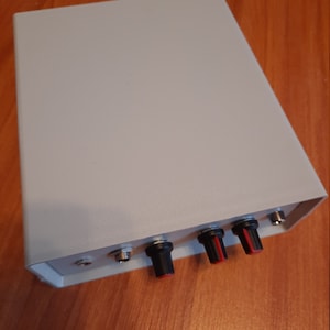 May include: A grey metal box with three black knobs and red accents. The box has two jacks on the side.