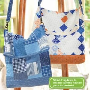 May include: Two quilted fabric bags, one blue and white, the other white with orange and brown accents. Both bags have a flap closure and a long strap. The bags are hanging on a wooden easel. The text "Kimberly's Sack: Remix" is at the top of the image.