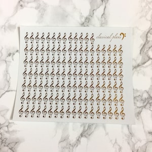 Op de afbeelding: Een vel met gouden vioolsleutel stickers op een witte achtergrond. Het vel heeft de tekst "classical plans" en een muzieknotensymbool.