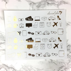 May include: A sheet of gold and white stickers with various icons, including a car, a house, a movie ticket, a suitcase, a lightbulb, a bathtub, a gift, a camera, a paw print, a money bag, a clock, an aeroplane, and a pair of glasses. The text "classical plans" is written in cursive at the top of the sheet.