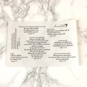 以下が含まれることがあります： イエス・キリストの誕生に関する聖書の詩句が書かれた白いカード。マタイ、イザヤ、ルカ、ヨハネからの詩句が含まれています。カードには、音符と「classical plans」という文字が書かれた装飾的なデザインが施されています。