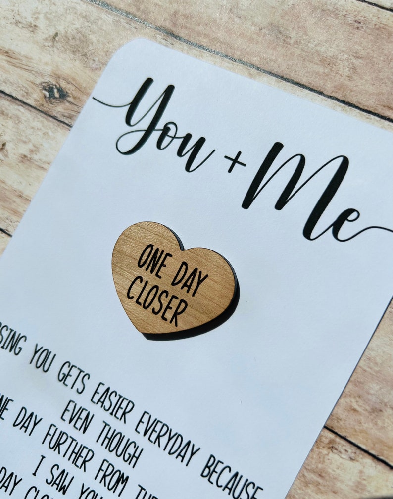 May include: A white card with black text that reads "You + Me" and a wooden heart with the text "One Day Closer".