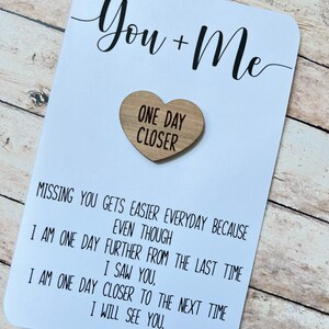 May include: White card with black text that reads "You + Me" and a wooden heart with the text "One Day Closer". The card reads "Missing you gets easier everyday because even though I am one day further from the last time I saw you, I am one day closer to the next time I will see you."