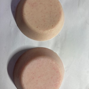 May include: Two round, pale pink soap bars with a textured surface. The soap bars have a subtle pink shimmer.