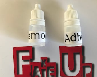 Op de afbeelding: Twee kleine witte flesjes met druppelaars. Het flesje links heeft een etiket met de tekst "Remove" en het flesje rechts heeft een etiket met de tekst "Adhesive".