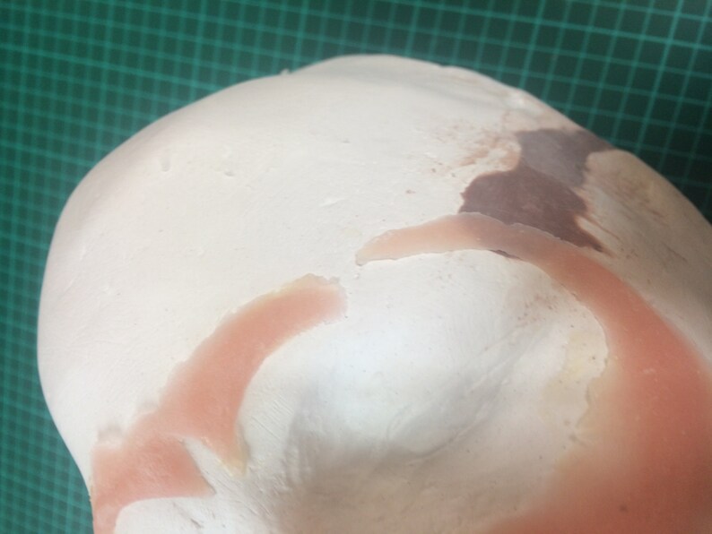May include: Close-up of a white, pink, and brown silicone mold for making a prosthetic ear. The mold is shaped like an ear and has a smooth, textured surface.