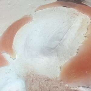 May include: Close-up of a white plaster mold with a pink silicone impression. The silicone impression is shaped like a curved line and has a rough texture.