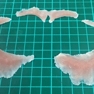 May include: Three pieces of clear, translucent, flesh-colored silicone, shaped like a crescent moon and a pair of wings.