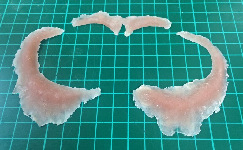 May include: Three pieces of clear, translucent, flesh-colored silicone, shaped like a crescent moon and a pair of wings.