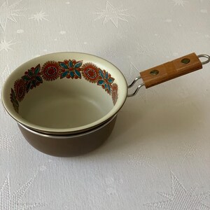 May include: A brown enamel saucepan with a white rim and a floral design around the top. The saucepan has a metal handle with a wooden grip.